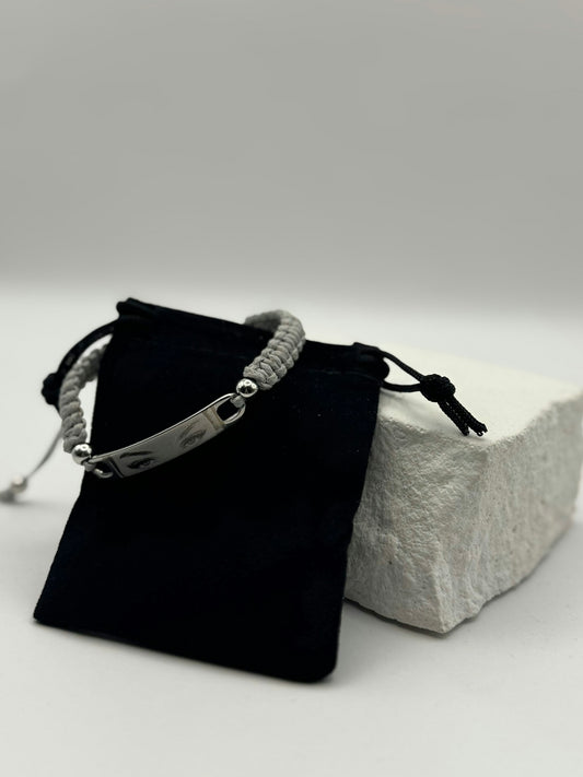 Gray braided bracelet with metal tag and pouch